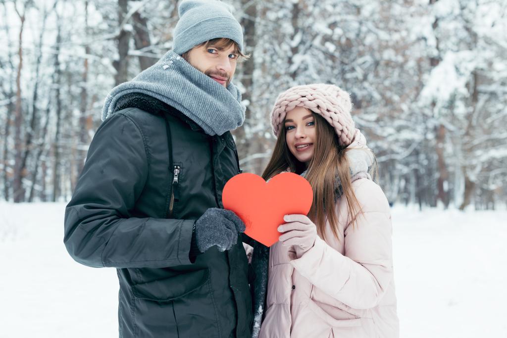 πορτρέτο του νεαρό ζευγάρι κρατώντας κόκκινη καρδιά στα χέρια μαζί στο χειμερινό πάρκο - Φωτογραφία, εικόνα