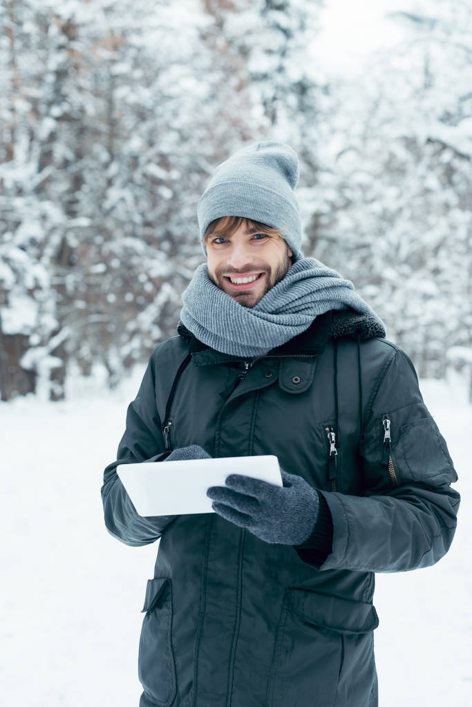 portrait of young smiling man with tablet looking at camera in winter park - Photo, Image
