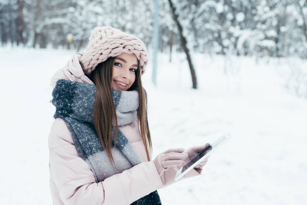 Seitenansicht einer lächelnden jungen Frau mit Tablet im Winterpark - Foto, Bild