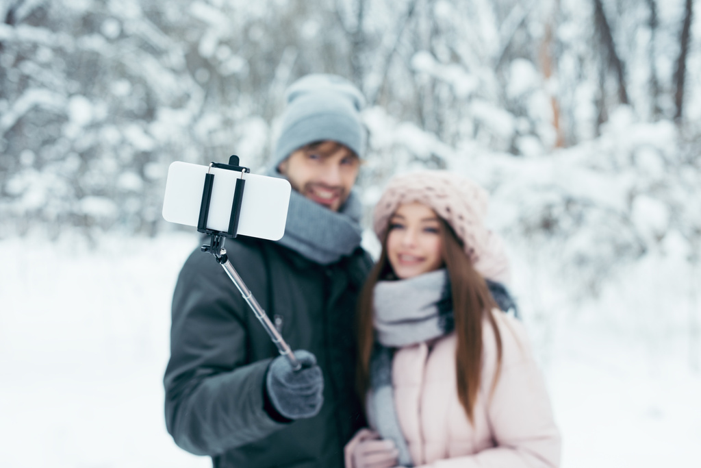 Selektiver Fokus eines lächelnden Paares beim gemeinsamen Selfie auf dem Smartphone im Winterpark - Foto, Bild