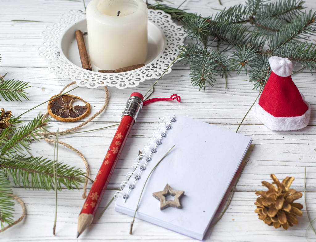 A festive winter mock up photo with a fir twigs, an opened note book, an old book, a pencil, cones, a candle and decation elements - Photo, Image