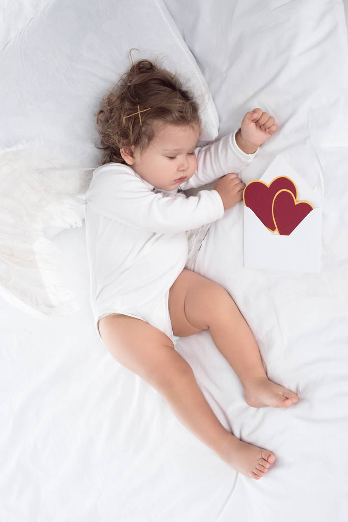маленький херувим с крыльями, лежащими на кровати с сердцами
  - Фото, изображение