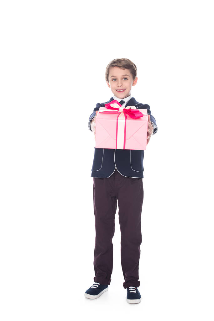schattig stijlvolle jongetje holding geschenkdoos en glimlachend op camera geïsoleerd op wit - Foto, afbeelding