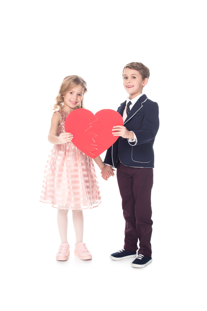 hermosos niños pequeños sosteniendo el símbolo del corazón rojo y sonriendo a la cámara aislada en blanco
  - Foto, Imagen