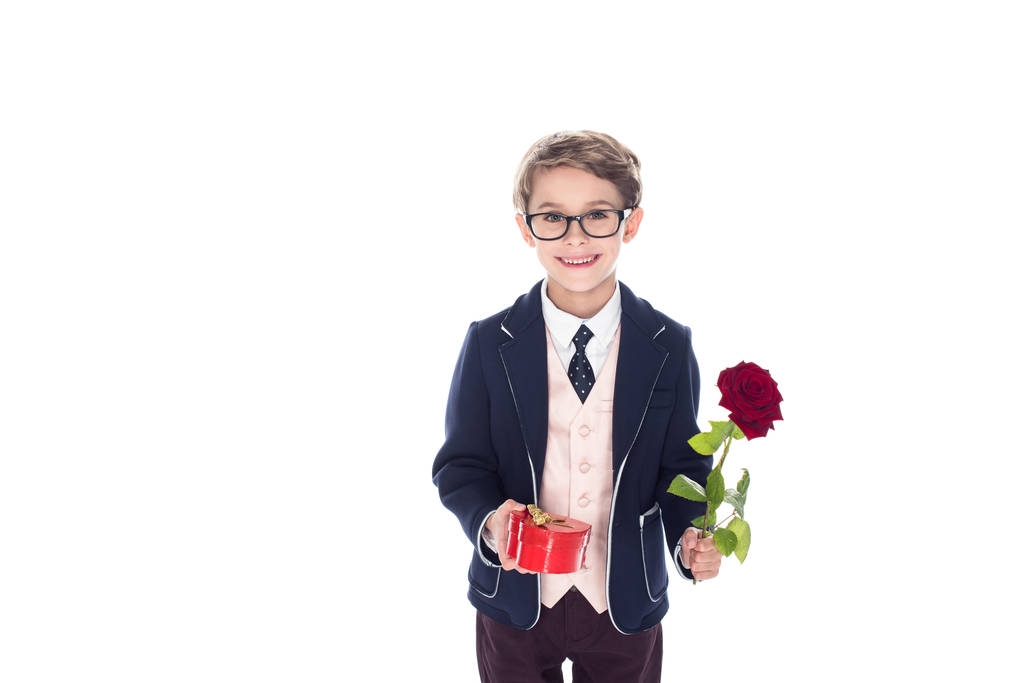 adorable little boy in suit and eyeglasses holding rose flower and heart shaped red gift box isolated on white - Photo, Image