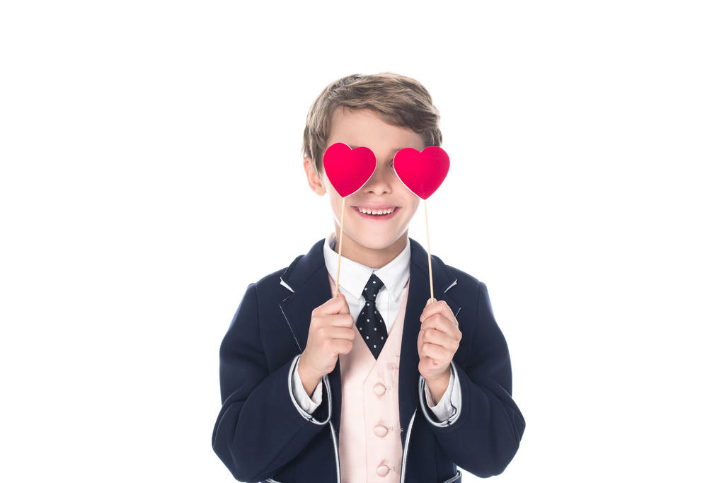 milý usměvavý chlapeček v obleku drží červené srdce na hole izolované na bílém - Fotografie, Obrázek