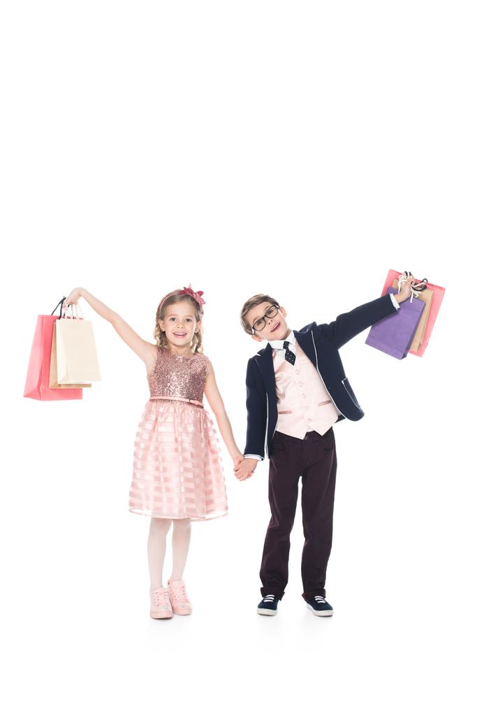 adorables niños pequeños sosteniendo bolsas de compras y sonriendo a la cámara aislada en blanco
 - Foto, Imagen