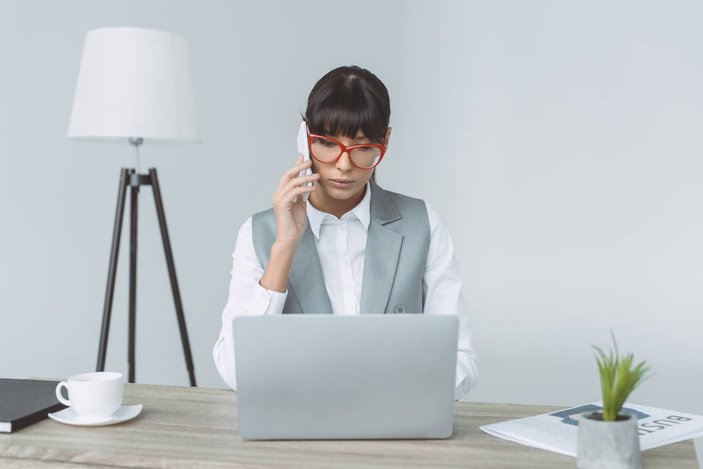 mujer de negocios hablando por teléfono inteligente y el uso de ordenador portátil aislado en gris
 - Foto, imagen