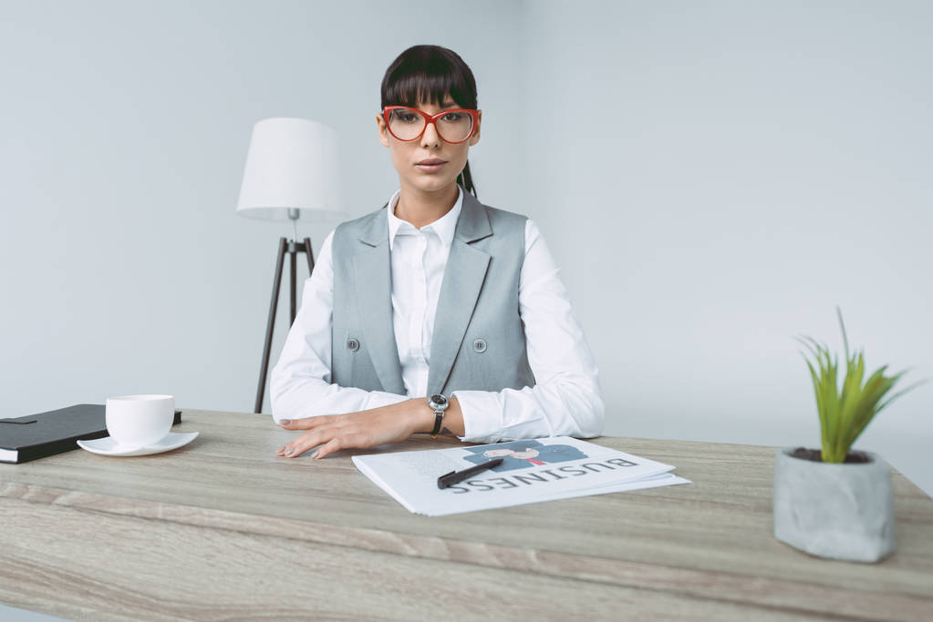 mujer de negocios sentada en la mesa de trabajo y mirando a la cámara aislada en gris
 - Foto, imagen