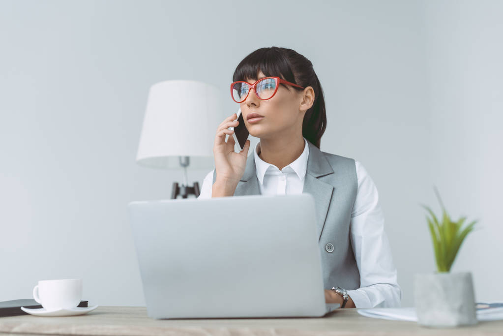 mujer de negocios hablando por teléfono inteligente y el uso de ordenador portátil aislado en gris
 - Foto, imagen