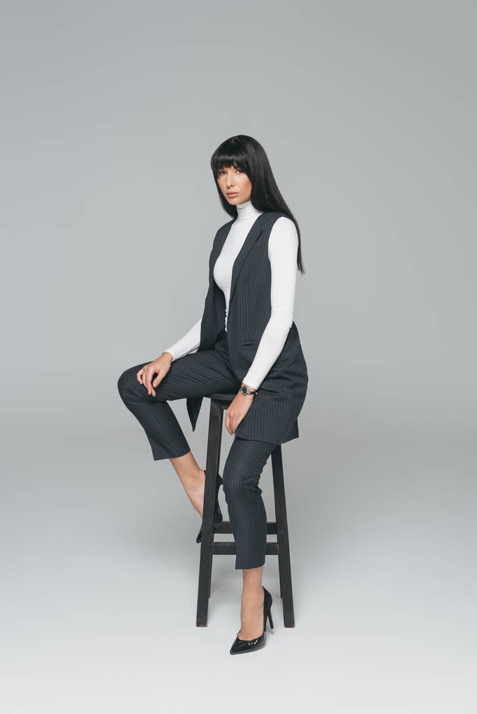 attraente bruna donna seduta sulla sedia nera su grigio
 - Foto, immagini