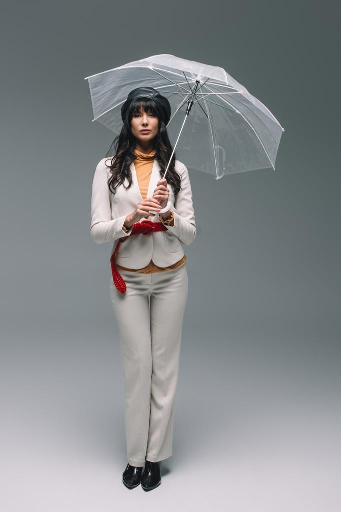Μελαχρινή γυναίκα με λευκό κοστούμι στέκεται με ομπρέλα σε γκρι - Φωτογραφία, εικόνα