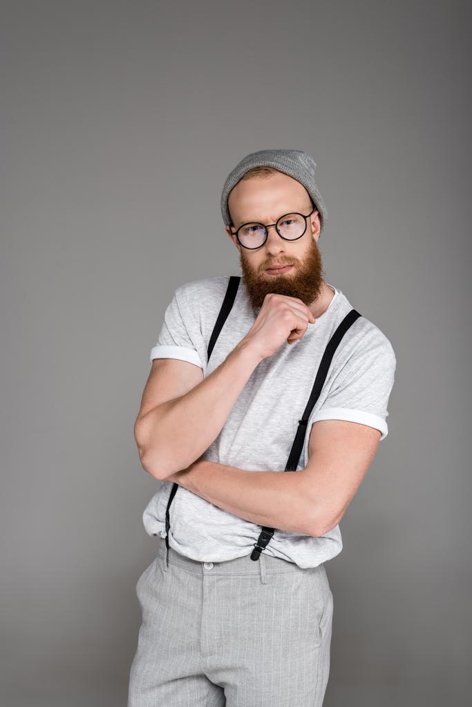 портрет стильного бородатого мужчины в подтяжках, смотрящего на камеру, изолированную на сером
 - Фото, изображение