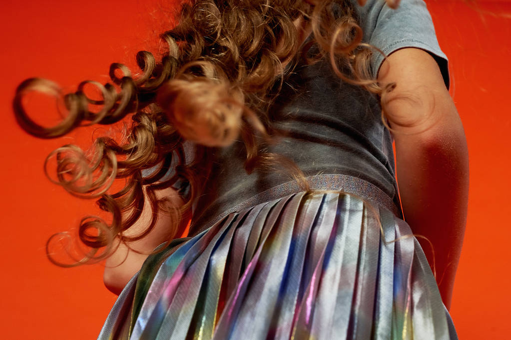 Κορίτσι σε πορτοκαλί φόντο στο στούντιο. Πολύ μακριά σγουρά μαλλιά σαν σε παραμύθι. Ραπουνζέλ. ανάπτυξη του κινήματος - Φωτογραφία, εικόνα