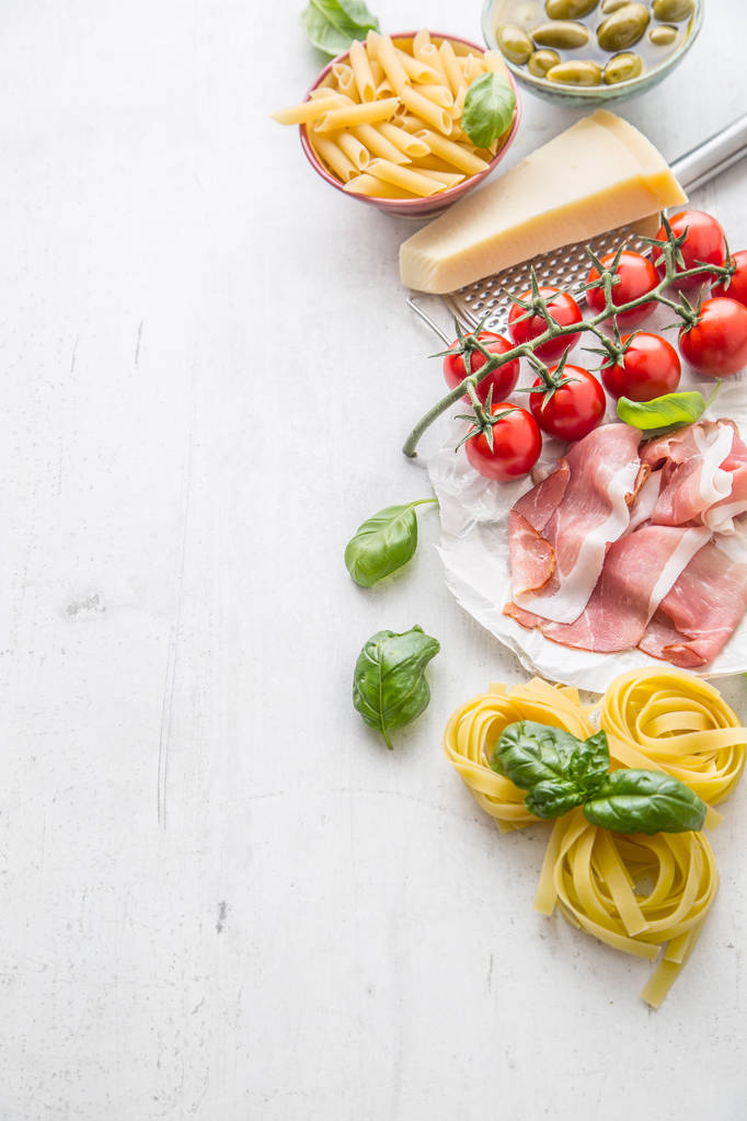 Італійський або середземноморської харчових кухня та інгредієнти на білий конкретні таблиці. Тальятелле Пєнє паста оливки оливкова олія помідори пармезан сир прошутто та базиліком накладає на конкретні дошки - Фото, зображення