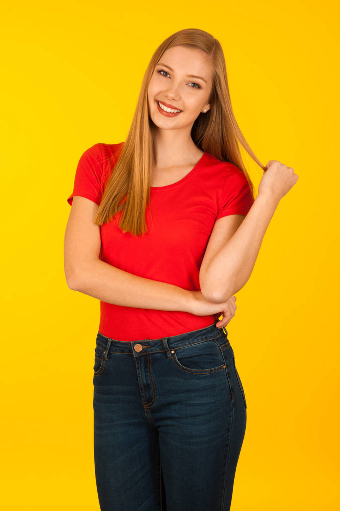 schöne junge Frau in rotem T-Shirt und Jeans über gelbem Backgr - Foto, Bild