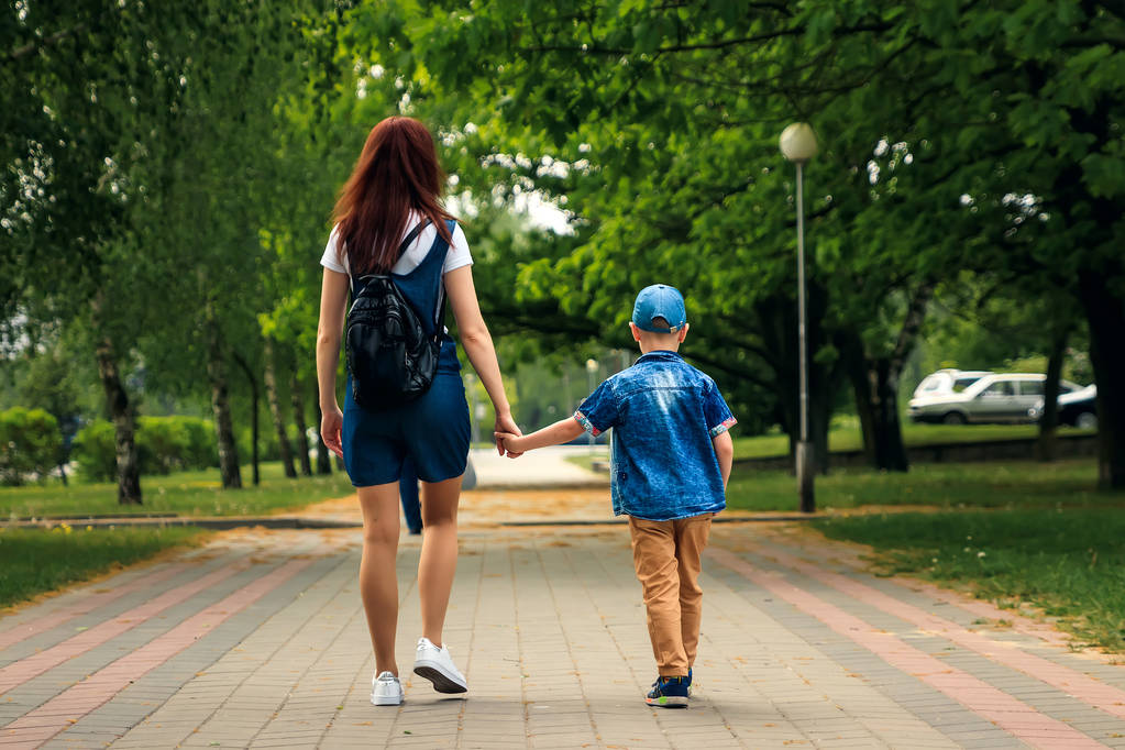 Egy fiatal anya és a fia séta a gyönyörű nyári park. Egy fiú és egy gyönyörű nő gyaloglás és birtoklás móka. Családi portré a szabadban. - Fotó, kép