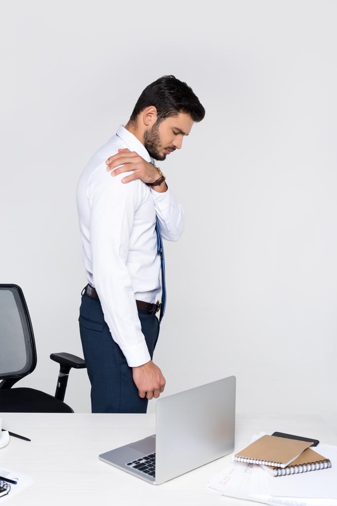 вид збоку молодого бізнесмена, який страждає від болю в плечі, стоячи на робочому місці
 - Фото, зображення