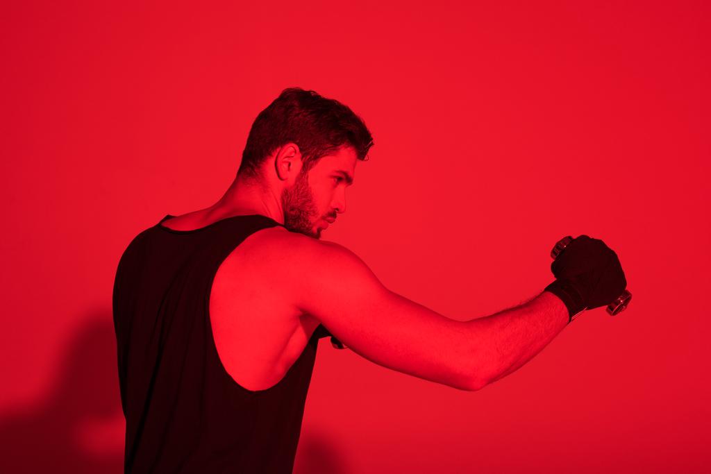 Seitenansicht eines jungen Kämpfers mit unter Rotlicht mit Bandagen bedeckten Händen - Foto, Bild