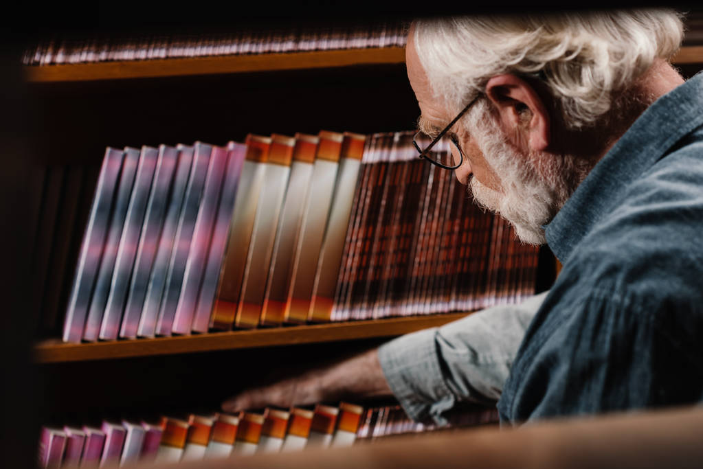 Bibliothekarin mit grauen Haaren sucht nach Buch - Foto, Bild