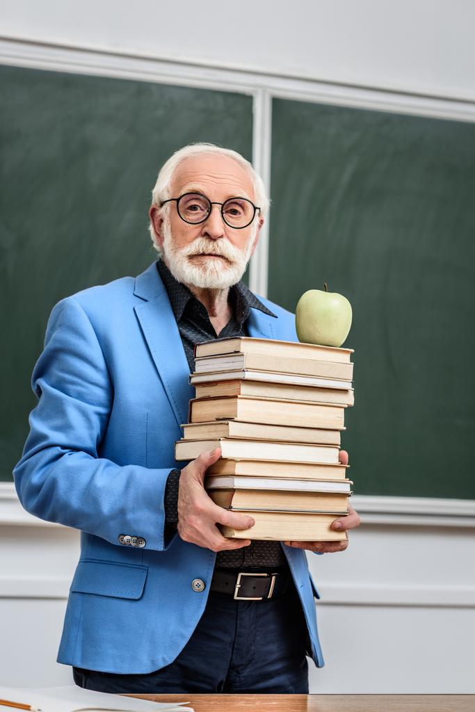 graue Haare Professor hält Stapel von Büchern mit Apfel auf dem Kopf - Foto, Bild