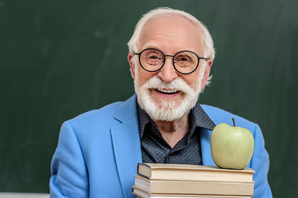 sonriente profesor de pelo gris sosteniendo pila de libros con manzana en la parte superior
 - Foto, imagen