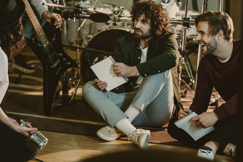 Musikband sitzt mit Notizblöcken auf dem Boden und redet - Foto, Bild
