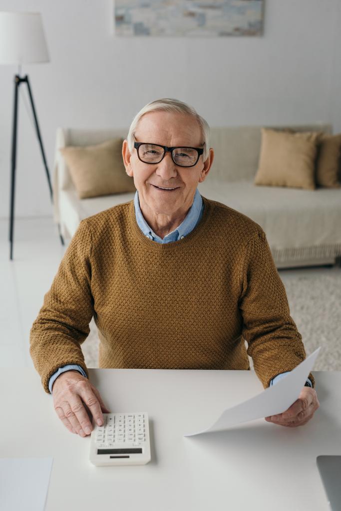 Senior selbstbewusster Mann benutzt Taschenrechner und hält leeres Papier - Foto, Bild