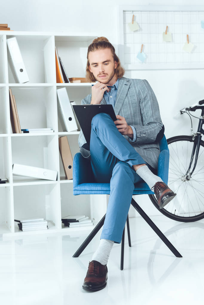 συλλογισμένος επιχειρηματίας ψάχνει στο Πρόχειρο και να κάθεται στην καρέκλα - Φωτογραφία, εικόνα