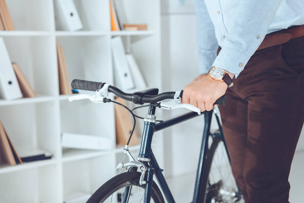 обрезанный образ бизнесмена, держащего велосипед в офисе
 - Фото, изображение