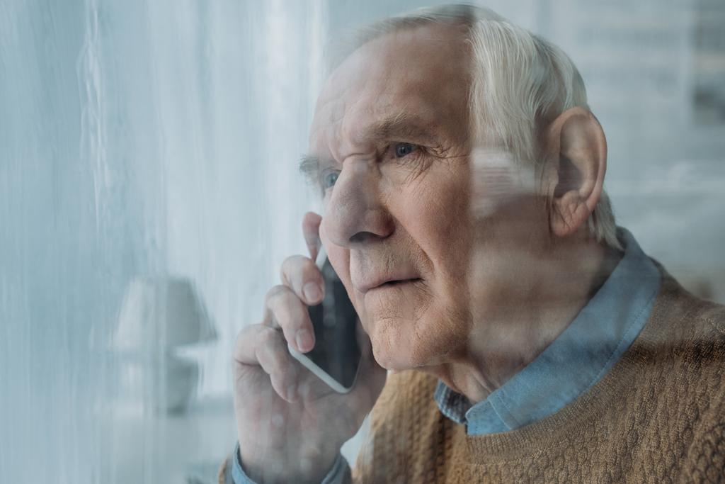 Derrière la vue en verre de l'homme dérangé âgé faisant un appel téléphonique
  - Photo, image
