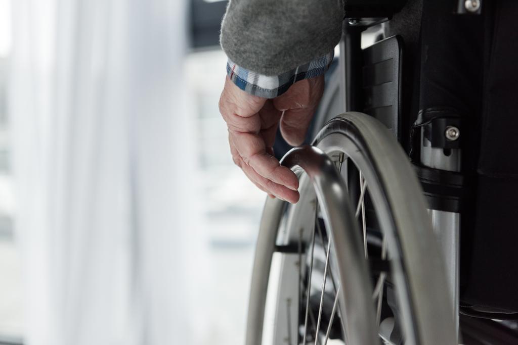 Bliska starszy człowiek z ręką na koła wózka inwalidzkiego - Zdjęcie, obraz