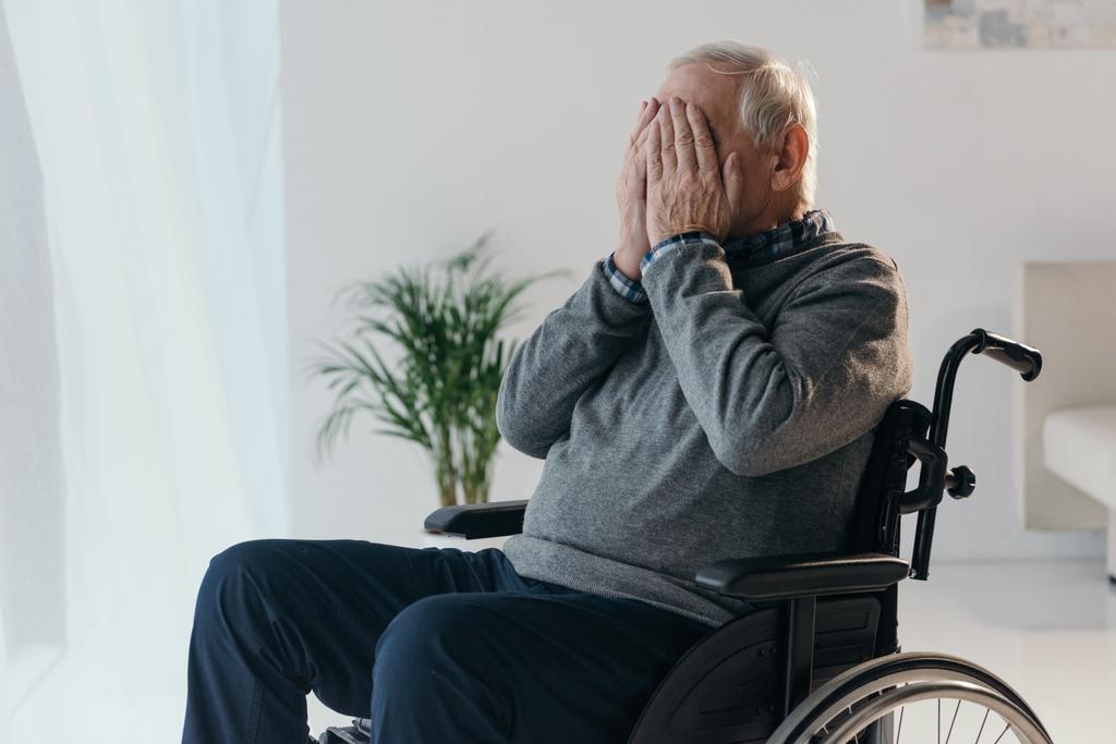 Hombre triste mayor en silla de ruedas cubriéndose la cara con las manos
 - Foto, Imagen