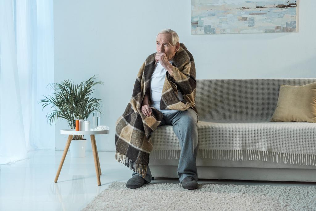 Хворий старший чоловік вкритий плоскими кашляками, сидячи диван в кімнаті з ліками на столі
 - Фото, зображення