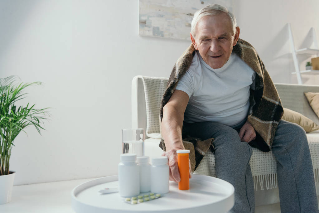 Vanhempi sairas mies peitetty ruudullinen ottaa lääkkeitä pöydästä
 - Valokuva, kuva