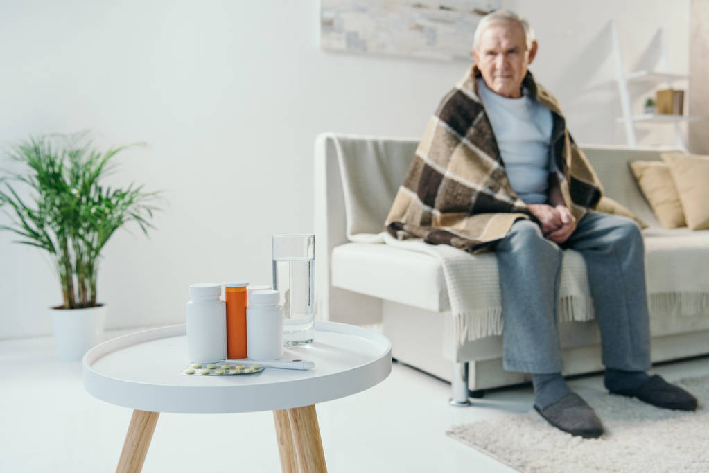 Senior réfrigéré homme couvert de plaid regarde les médicaments sur la table
 - Photo, image