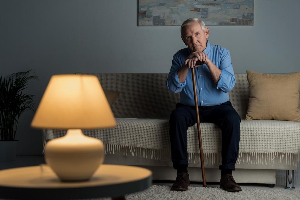 Hombre mayor cansado se apoya en un bastón mientras está sentado en el sofá
 - Foto, Imagen
