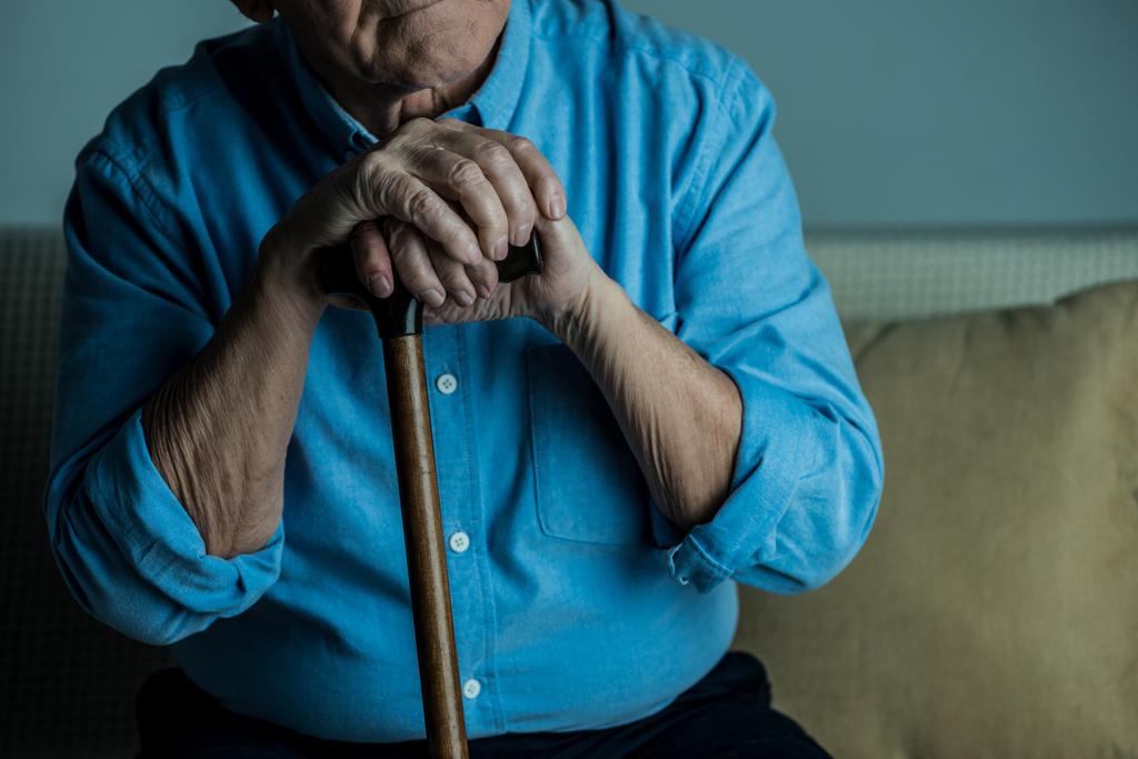 Крупный план пожилого человека опирается на трость, сидя на диване
 - Фото, изображение