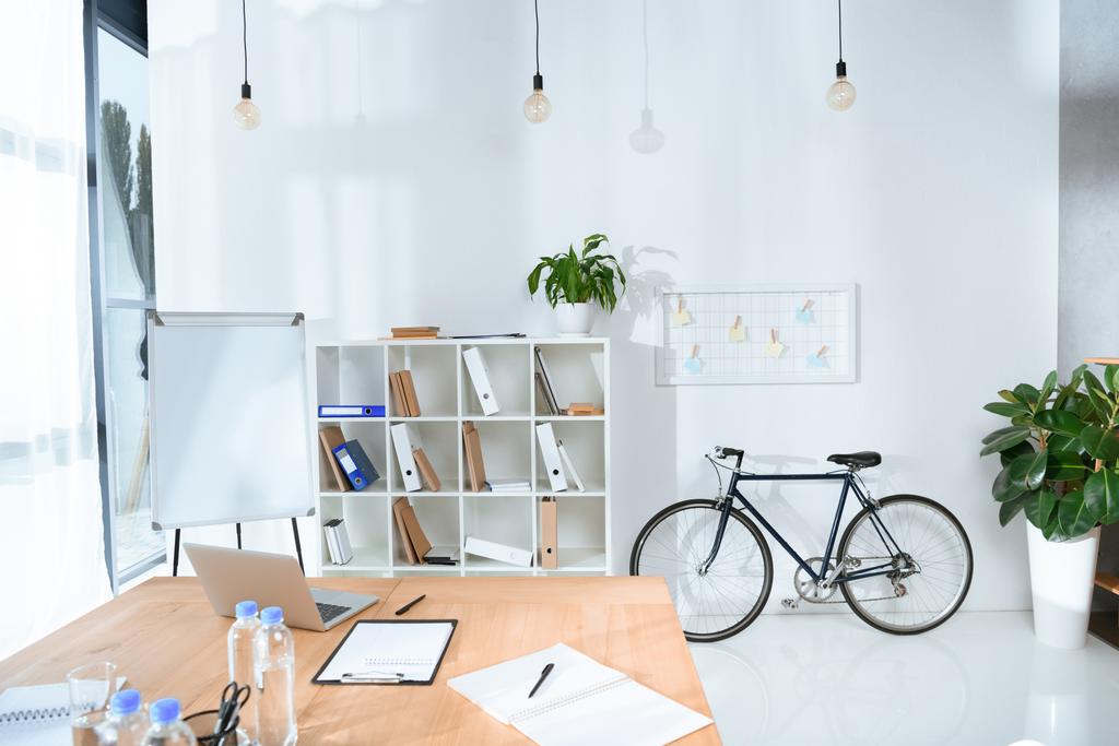 вид на пустой офисный интерьер со столом и велосипедом напротив стены
  - Фото, изображение