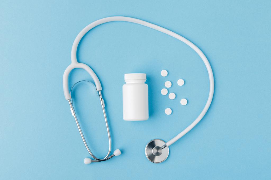 stethoscope, scattered pills and package isolated on blue background - Photo, Image