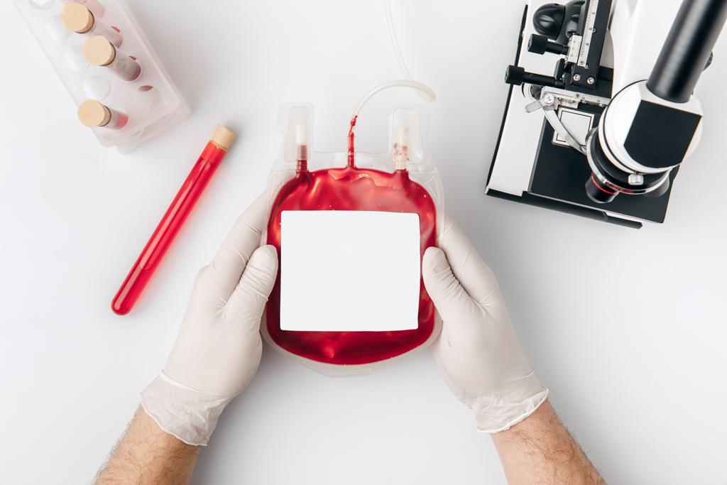 Ellerin kan transfüzyonu şişeleri ve beyaz arka plan üzerinde izole mikroskop için elinde eldiven Üstten Görünüm    - Fotoğraf, Görsel