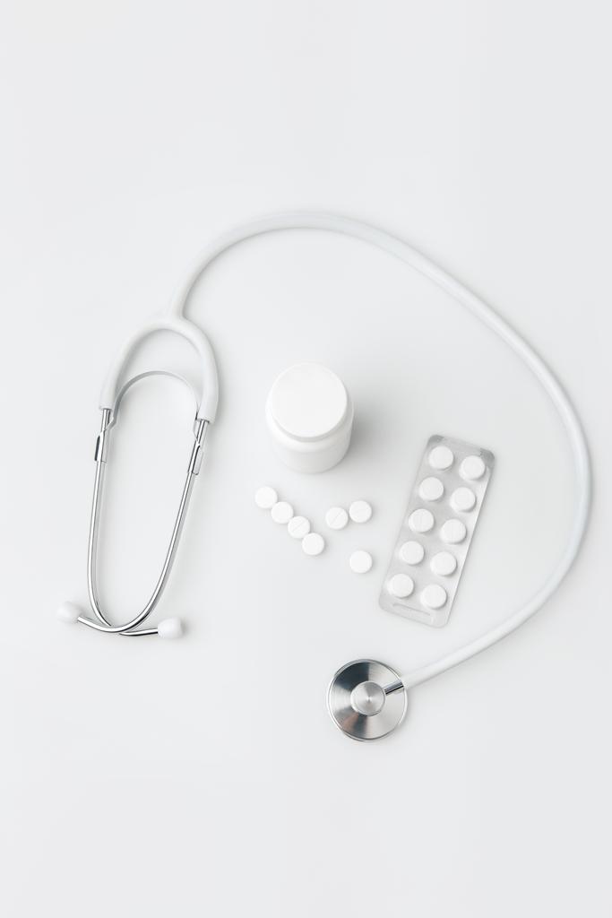 Stethoskop, verstreute Pillen und weitere Tabletten in Verpackung und Plastikdose isoliert auf weißem Hintergrund     - Foto, Bild