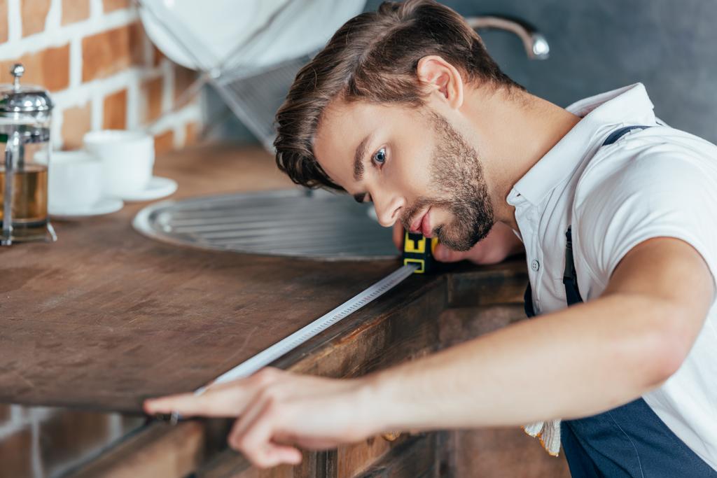 professionnel jeune homme à tout faire mesurant meubles de cuisine avec ruban adhésif
 - Photo, image