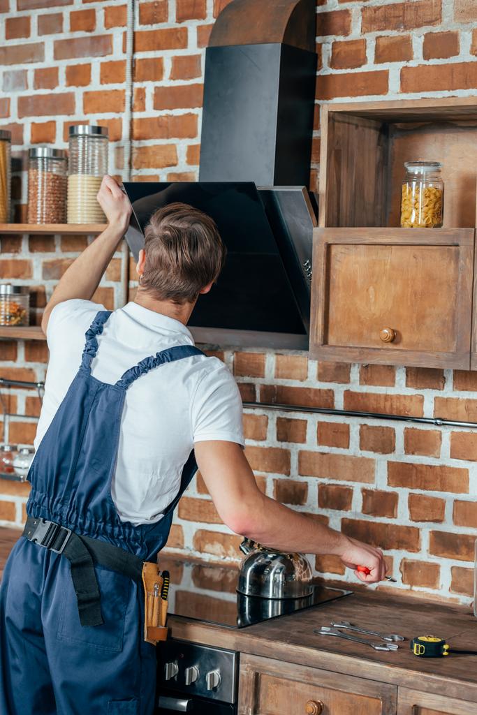 Вид сзади молодого разнорабочего, закрепляющего капюшон на кухне
 - Фото, изображение