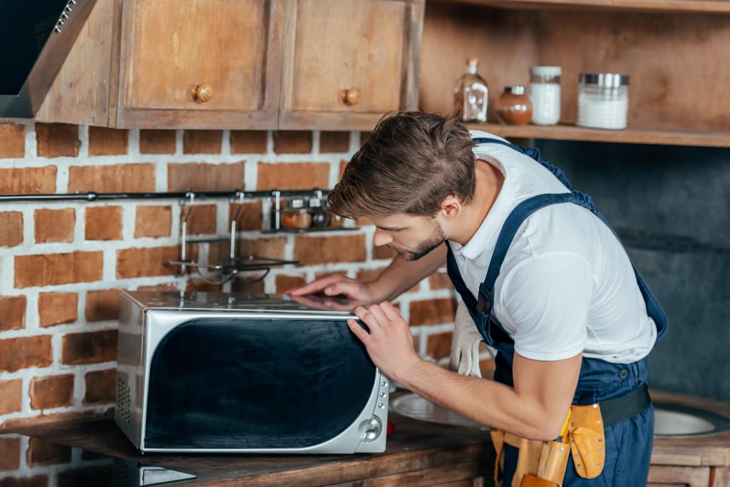 професійний молодий майстер ремонтує мікрохвильову піч на кухні
  - Фото, зображення