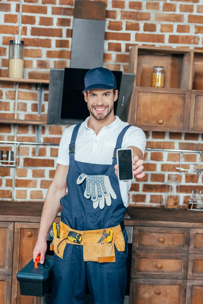 Lächelnder junger Hausmeister mit Smartphone und Werkzeugkiste - Foto, Bild