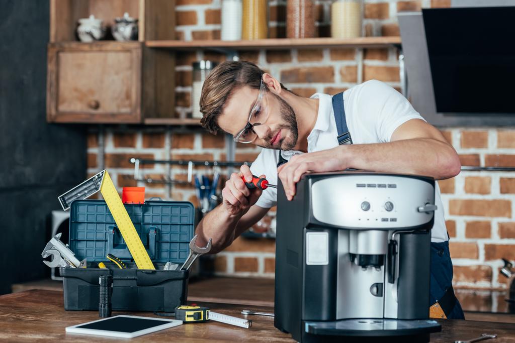 επαγγελματίας νεαρός επισκευαστής σε μηχανή καφέ για τη στερέωση γυαλιών  - Φωτογραφία, εικόνα