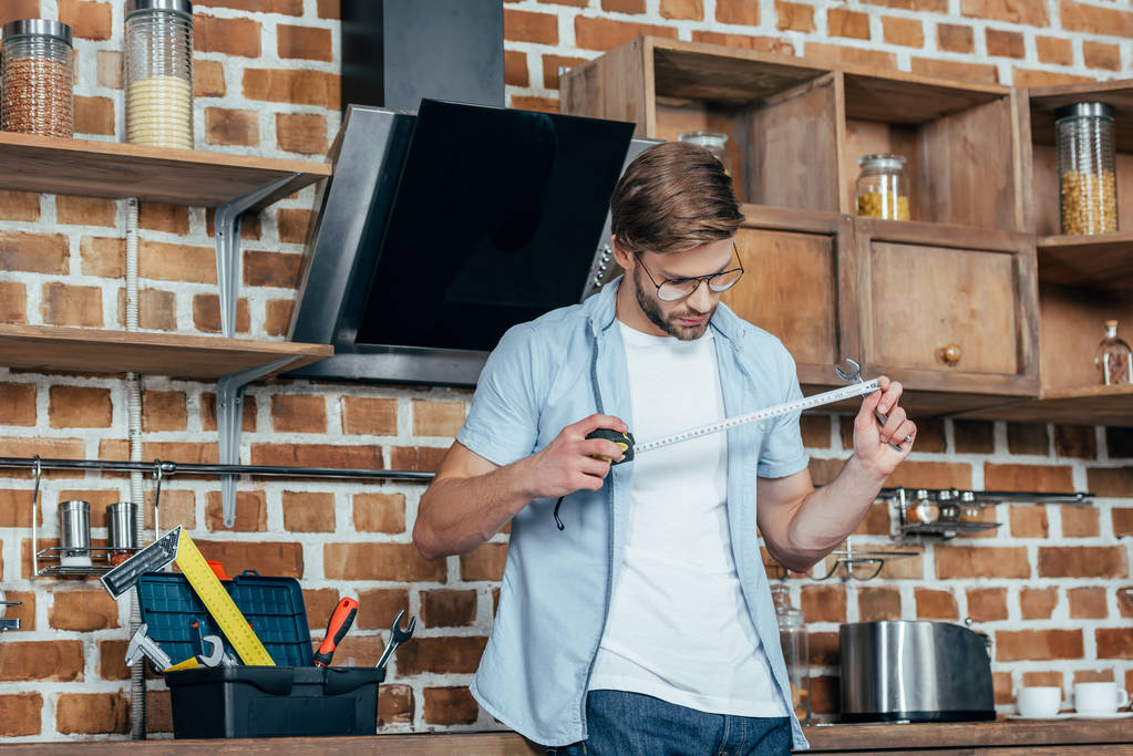 молодой человек держит измерительную ленту во время ремонта кухонного капюшона
  - Фото, изображение