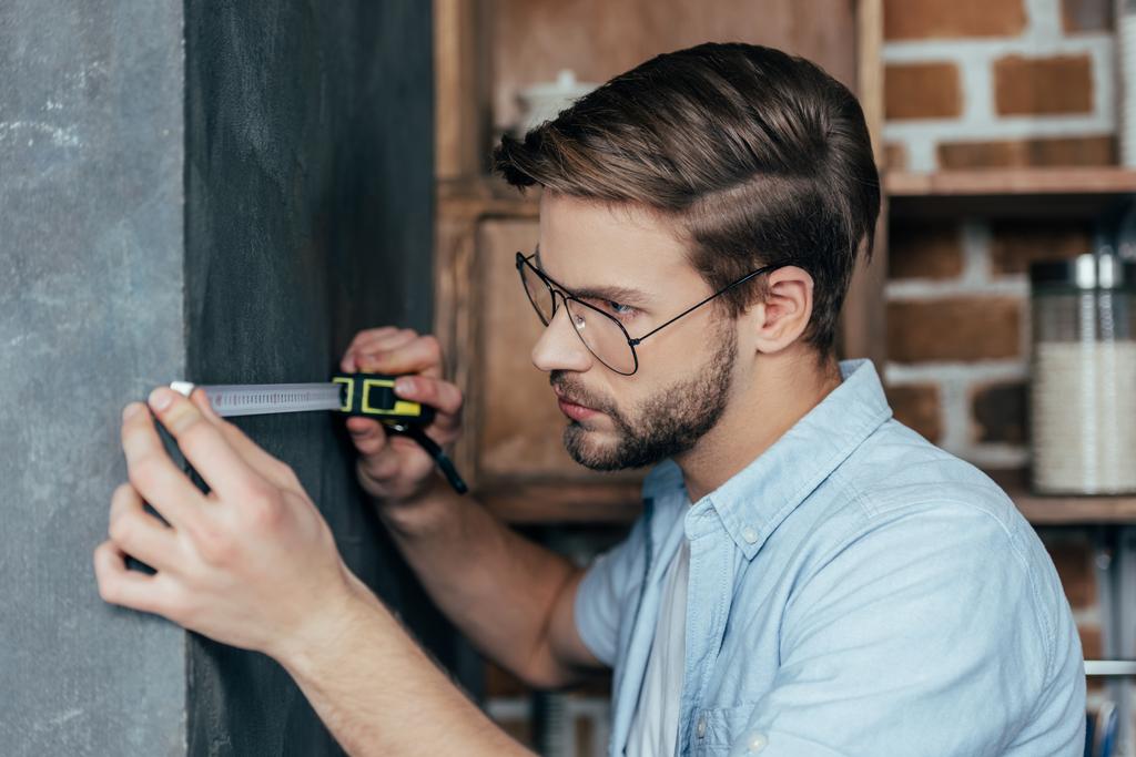 jonge man in brillen muur met tape thuis meten - Foto, afbeelding