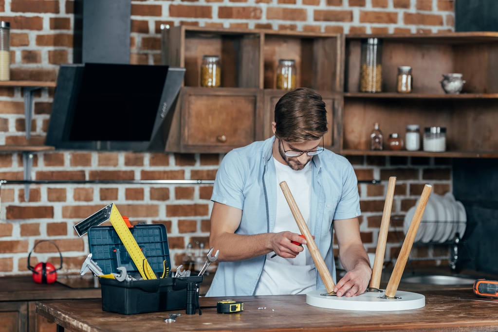 koncentruje się młody człowiek w okularach gospodarstwa śrubokręt i naprawianie stołek z śrubokręt  - Zdjęcie, obraz